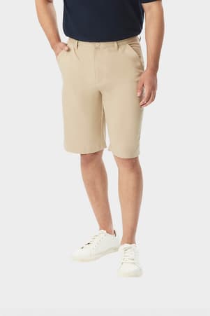 Man wearing khaki French Toast flat front stretch performance short, front view showing side pockets and above the knee length. of  Boys' Flat Front Stretch Performance Short