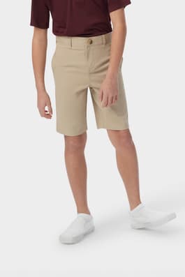 Boy wearing khaki French Toast boys' flat front stretch twill short, side pockets and above the knee length, front view. of  Boys' Flat Front Stretch Twill Short