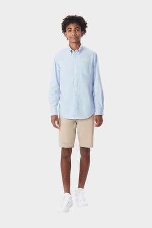 Young man wearing a blue French Toast long sleeve oxford shirt, front view showcasing detail and adult sizing.