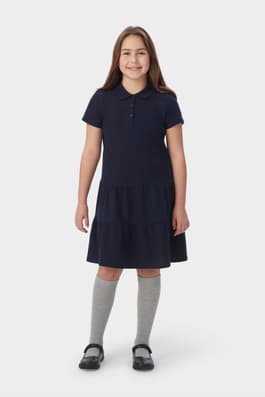 Front view of girl in navy French Toast short sleeve ruffle pique polo dress, showing 3 button placket and knit collar. of  Short Sleeve Ruffle Piqué Polo Dress