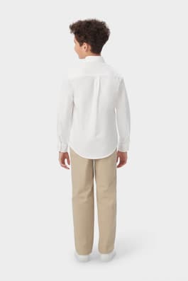 Back view of boy wearing white French Toast long sleeve oxford shirt, untucked to show shirttail hem and fit.