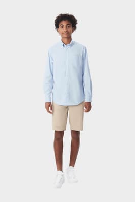 Young man wearing a blue French Toast long sleeve oxford shirt, front view showcasing detail and adult sizing.