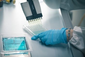 Closeup of the blue gloved hands of a scientist during a multichannel pipette test in a 96 well microplate