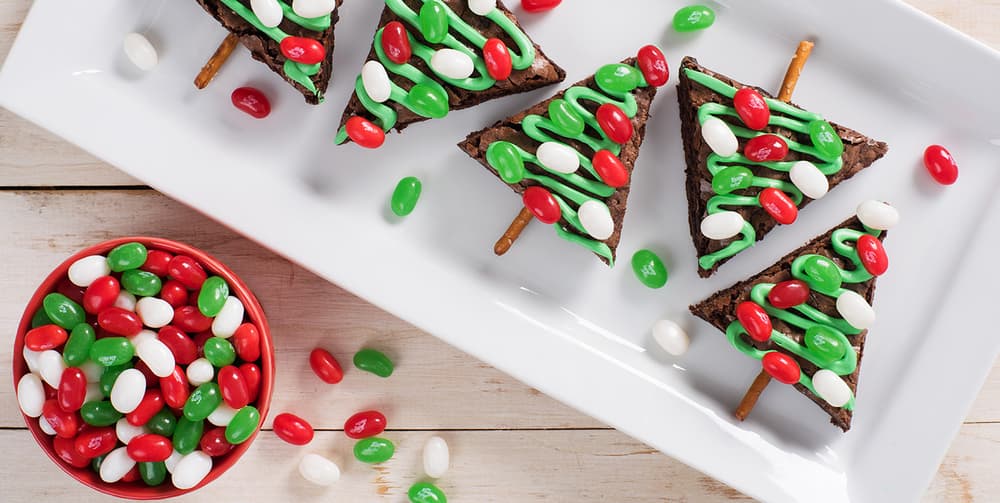 christmas tree brownies with green filling and jelly beans on top with a red bowl of jelly beans on the side