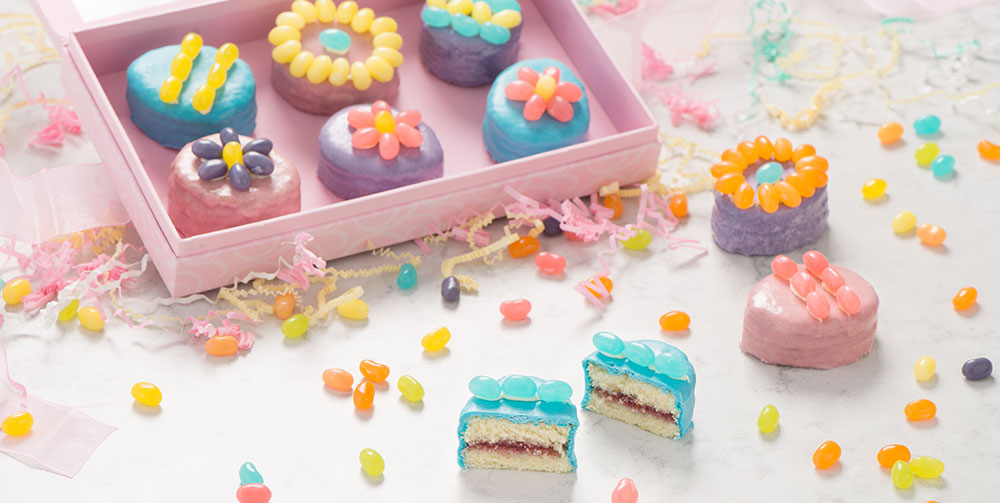 Open box of petit fours and assorted petit fours on a table.