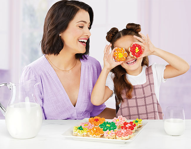 Mother and daughter sitting at table with homemade flower-shaped sugar cookies topped with jelly beans.