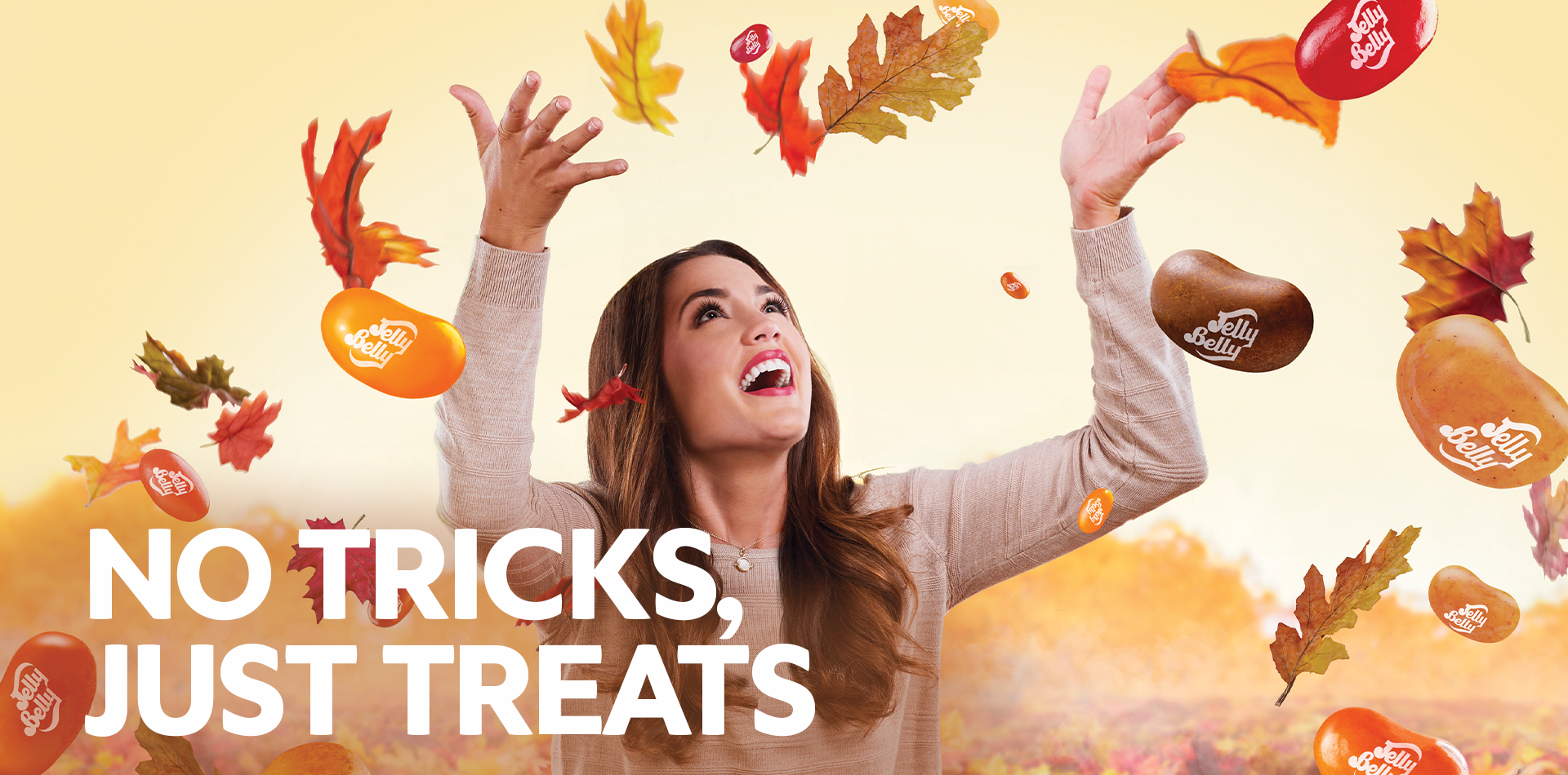 Woman tossing leaves and jelly beans in the air, with text No Tricks, Just Treats