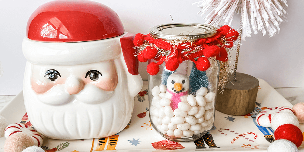 picture of Santa ceramic next to a jar filled with white Jelly Belly jelly beans, miniature snowman, and miniature christmas trees