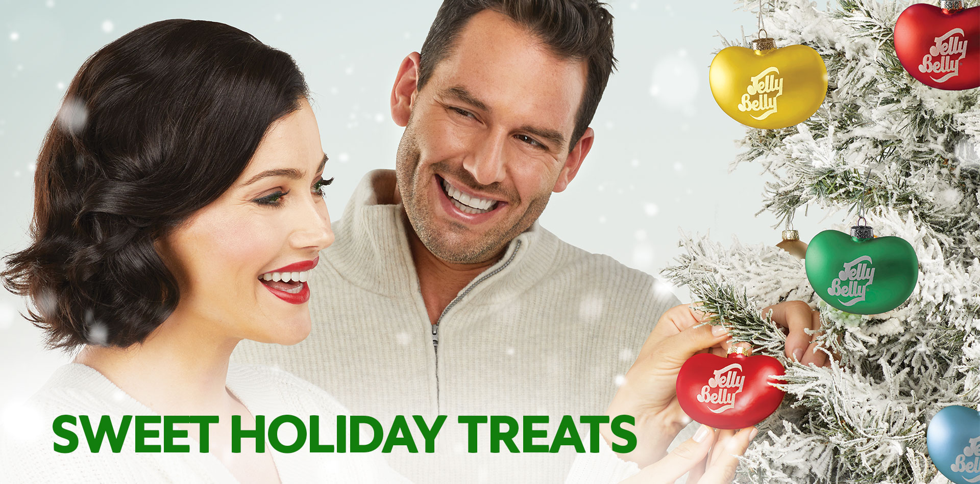 Man and woman decorating a Christmas Tree with jelly bean shaped ornaments, with text Sweet Holiday Treats