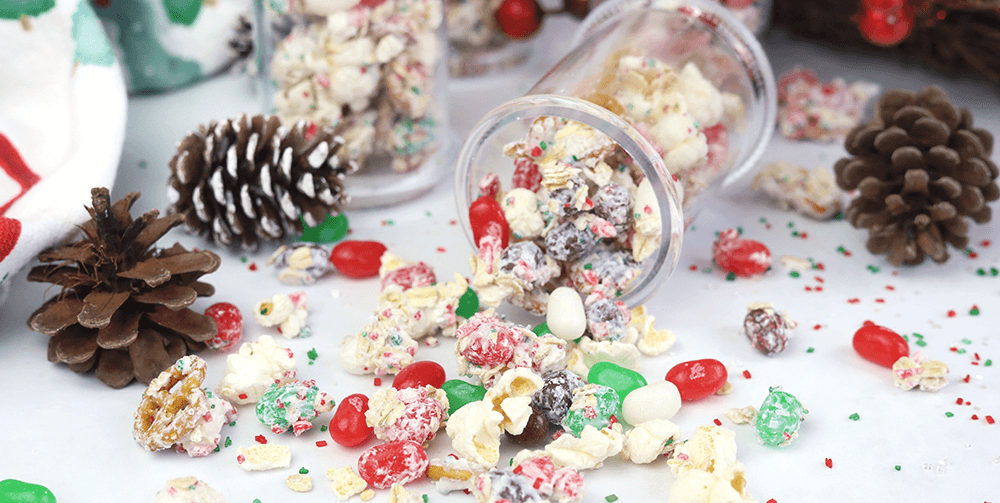 a jar tipped over and filled with popcorn, pretzels, white chocolate, and jelly belly jelly beans all covered with green and red sugar sprinkles