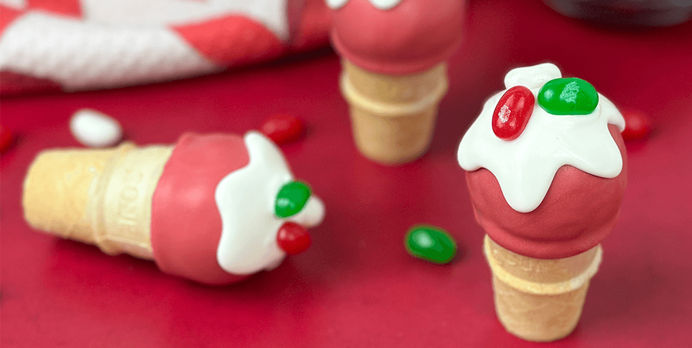 christmas cake made to look like a red ice cream scoop on a cone, topped with white frosting and red and green jelly beans