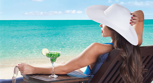 A women in a blue swimsuit and white sun hat sitting on the beach with a cocktail glass full of Margarita jelly beans