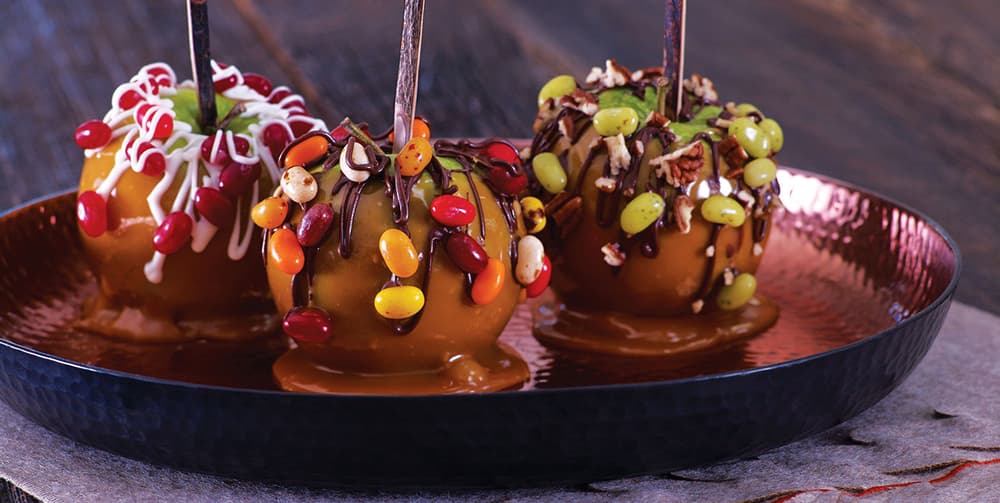 three caramel covered apples with jelly beans sprinkled onto it