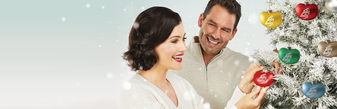 A man and woman standing next to a christmas tree with jelly belly ornaments.